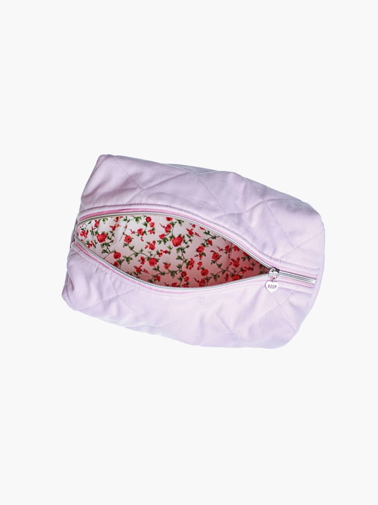Quilted pink makeup and toiletry bag with a silver zip with a heart logo zip pull, it is open revealing a floral lining. Set on a white background