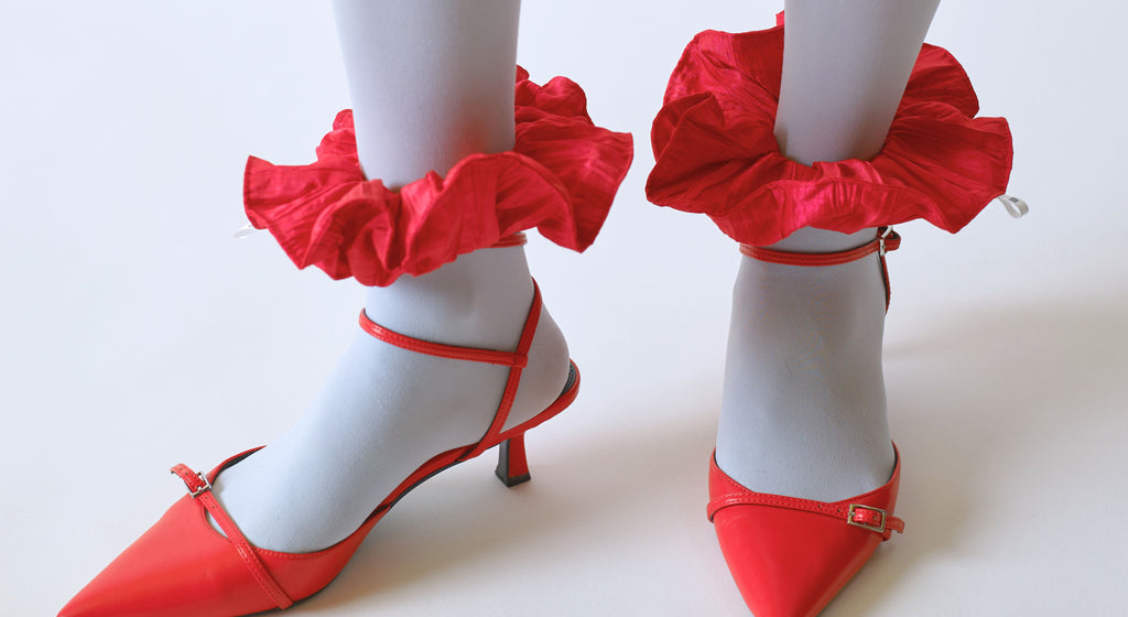 Red kitten heeled shoes , worn with pale blue tights and red scrunchie on each ankle, set  against a white background