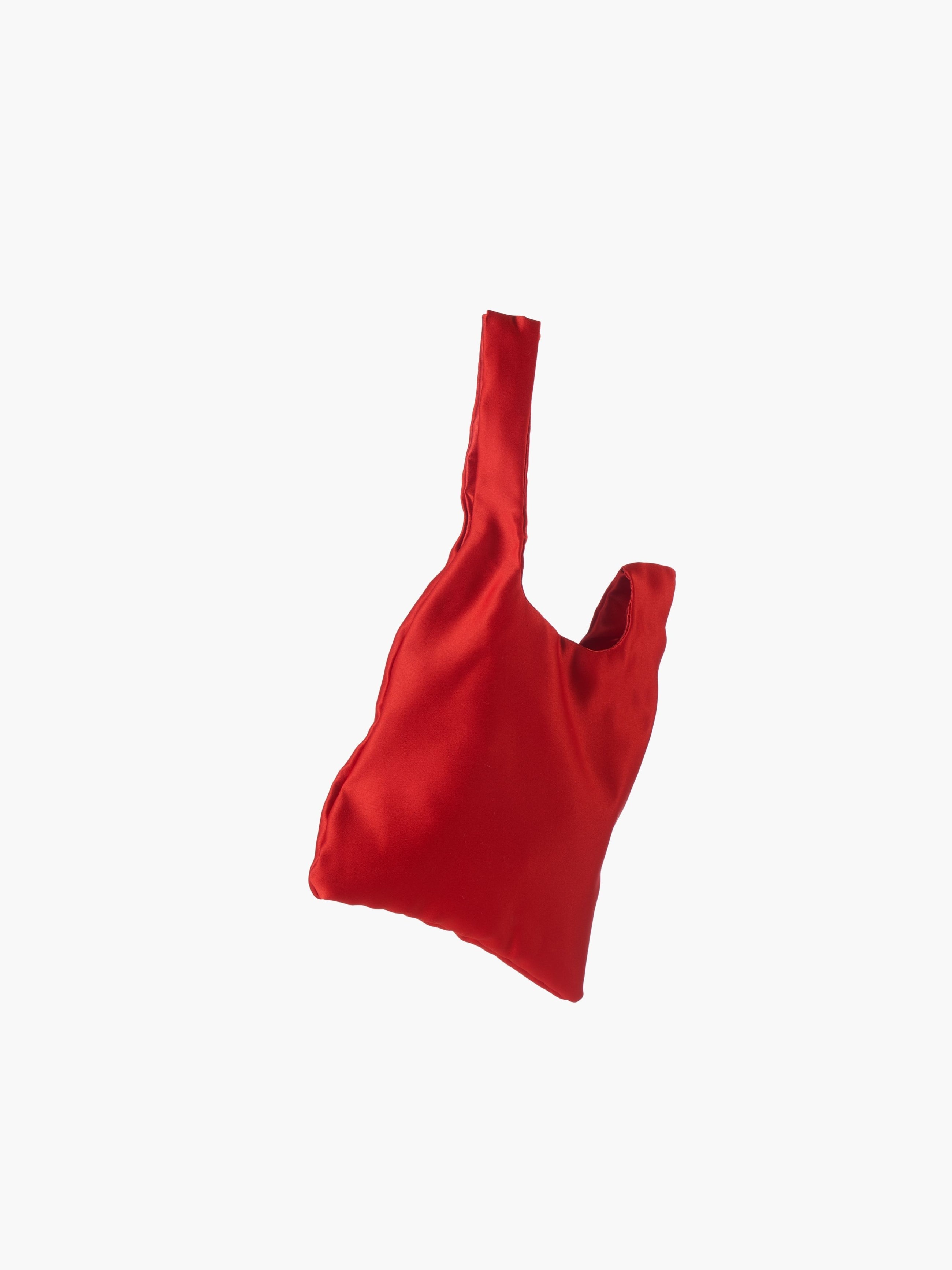 Red satin knot bag against a plain white background. The elegant bag has a twisted handle and sleek, glossy fabric, exuding a chic, minimalist style.