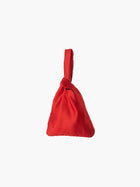 Red satin knot bag against a plain white background. The elegant bag has a twisted handle and sleek, glossy fabric, exuding a chic, minimalist style.