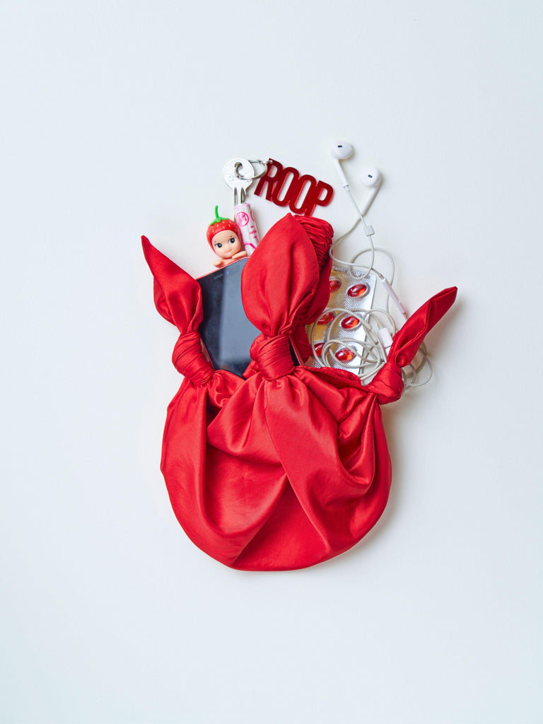 Red knotted bag with possessions spilling out including a small toy, keyring and earphones on a white background