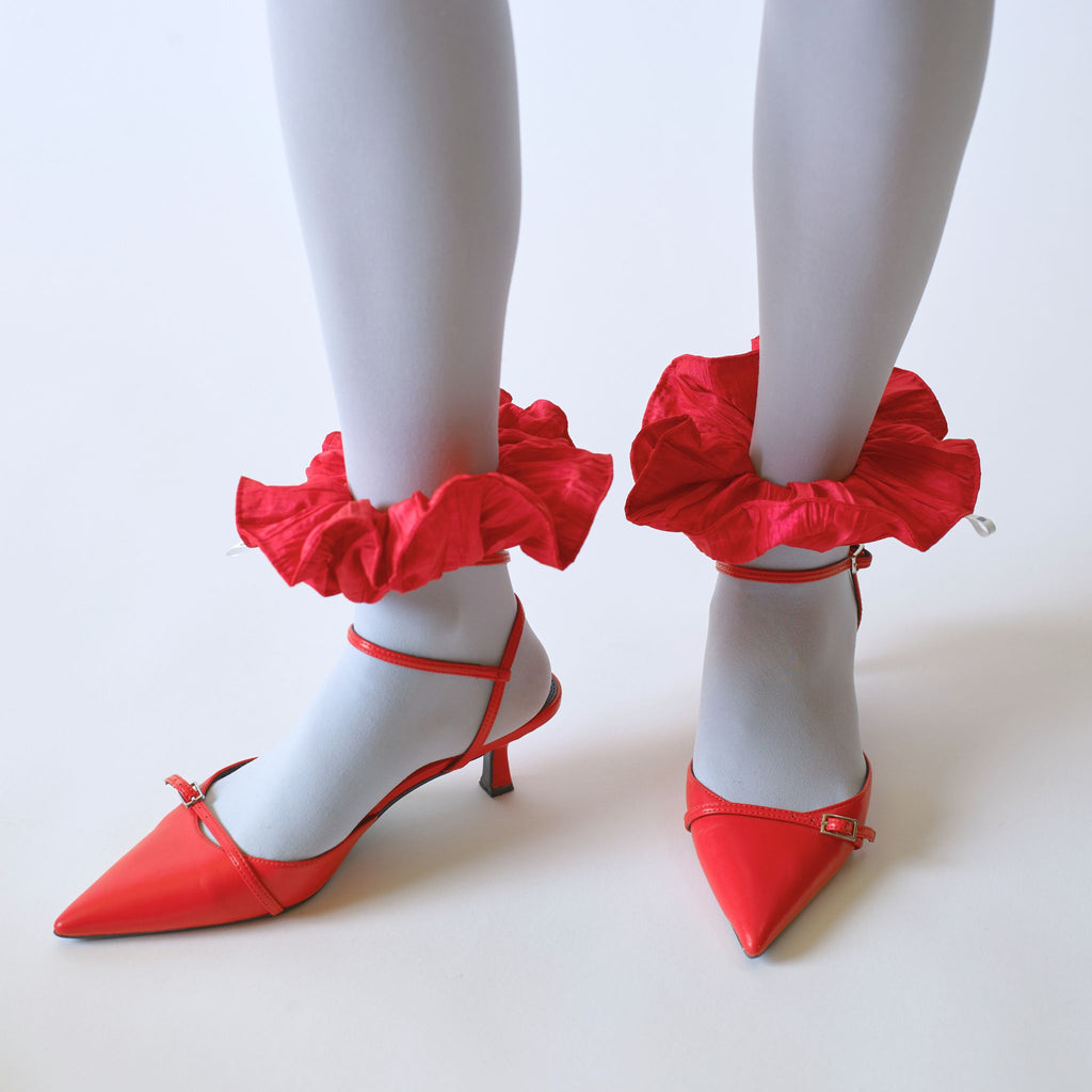 Red kitten heeled shoes , worn with pale blue tights and red scrunchie on each ankle, set  against a white background