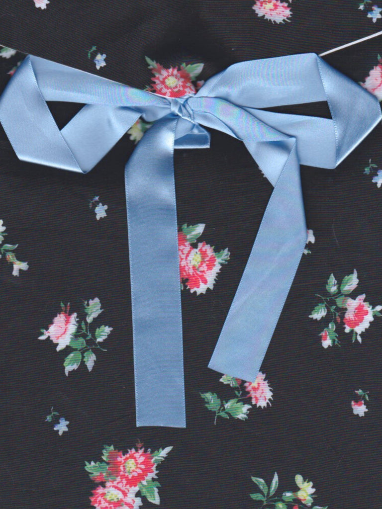 Close up of a black floral patterned fabric envelope pouch tied with a blue ribbon.