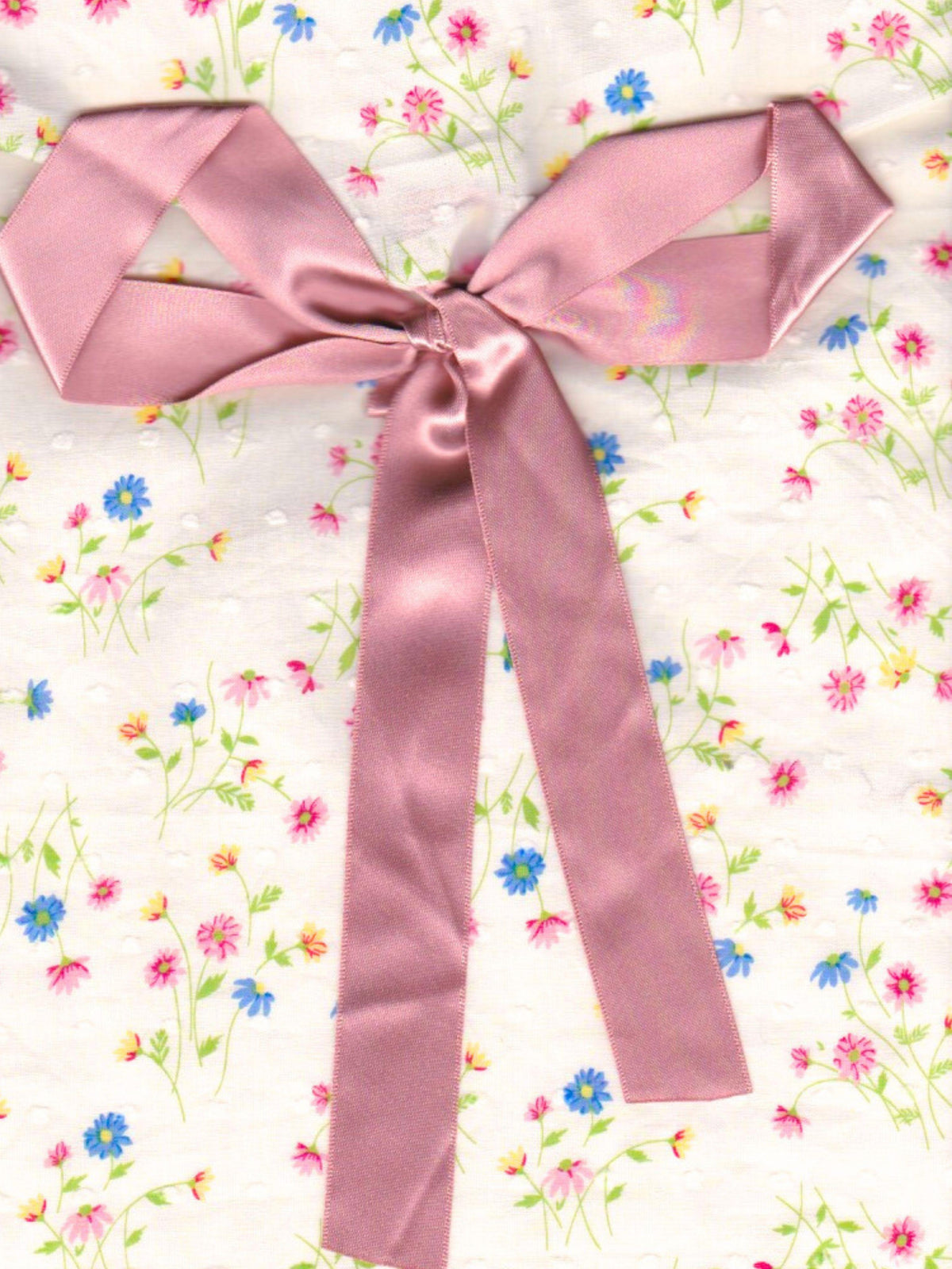 Close up of cream floral patterned fabric envelope pouch tied with a pink ribbon.