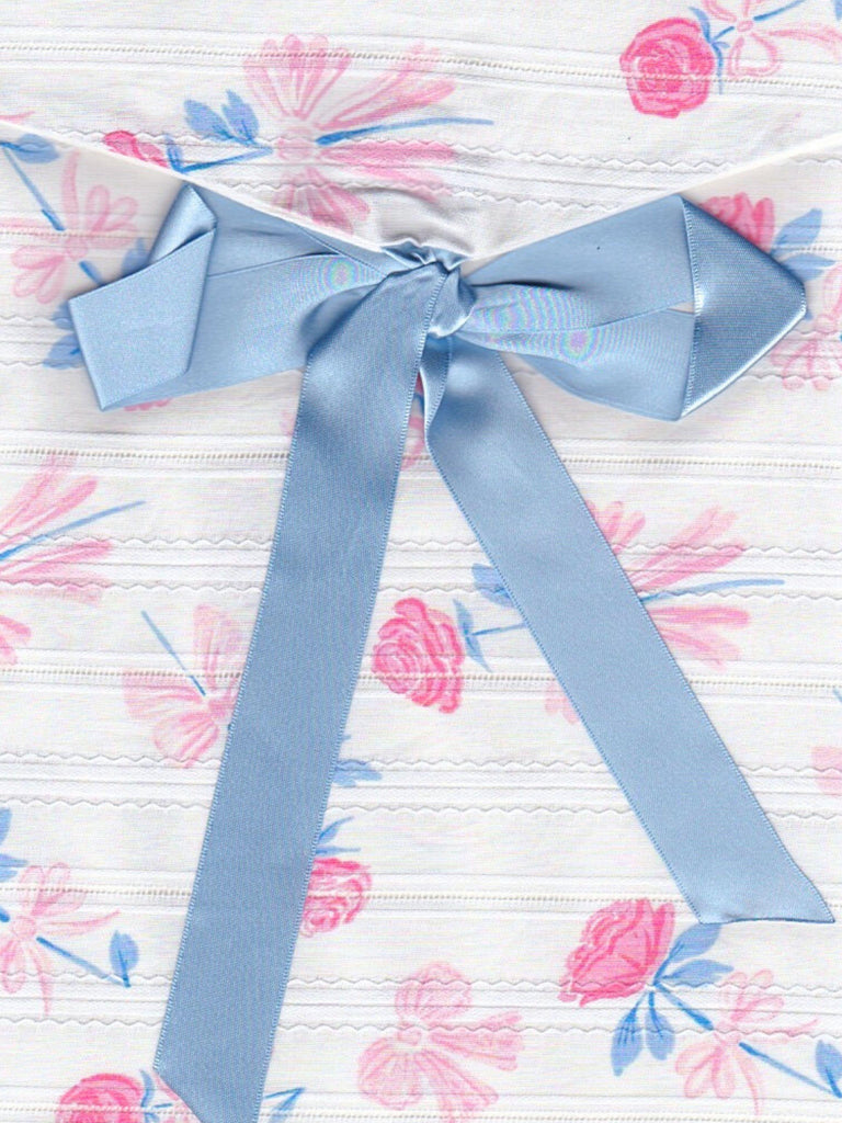 Close up of a floral print fabric envelope pouch with a blue ribbon on a white background