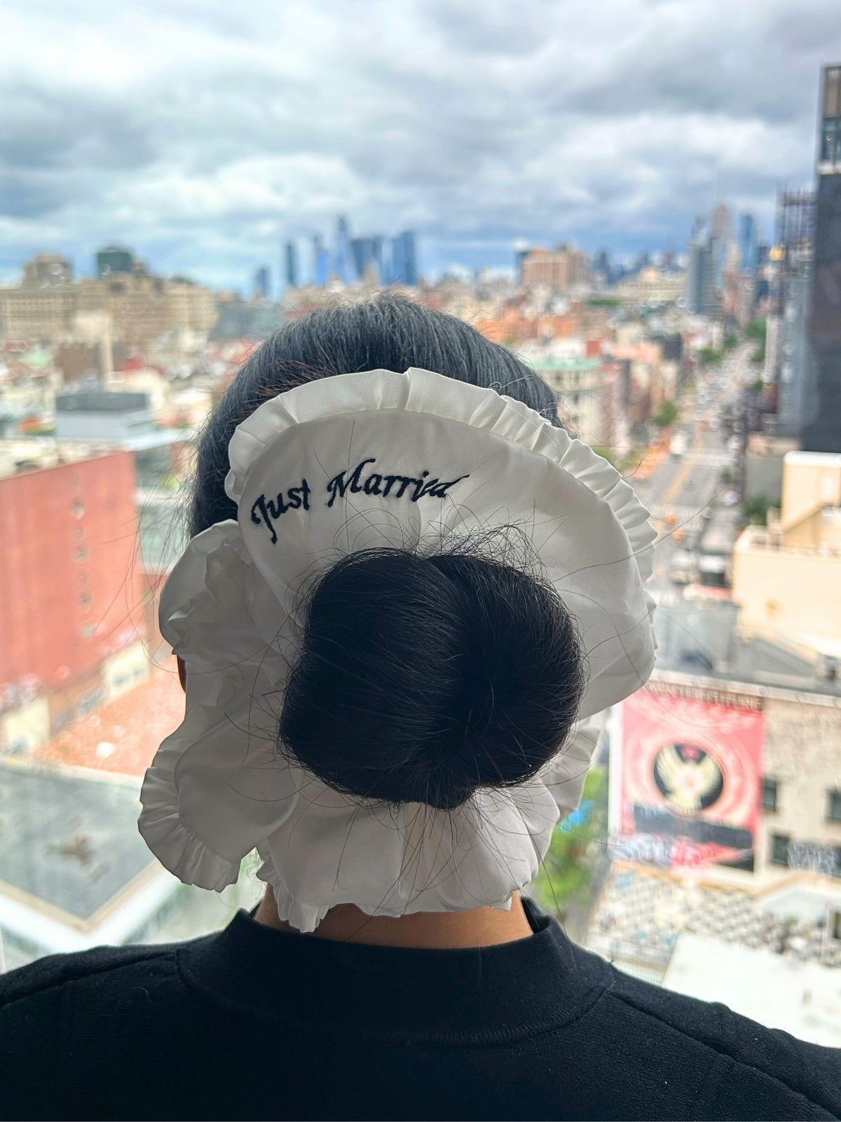 Person wearing a 'Just Married' ivory ruffle scrunchie with blurred new york cityscape in the background