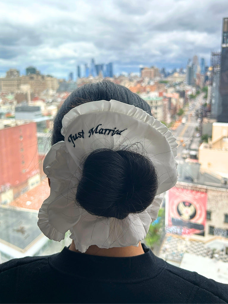Person wearing a 'Just Married' ivory ruffle scrunchie with blurred new york cityscape in the background