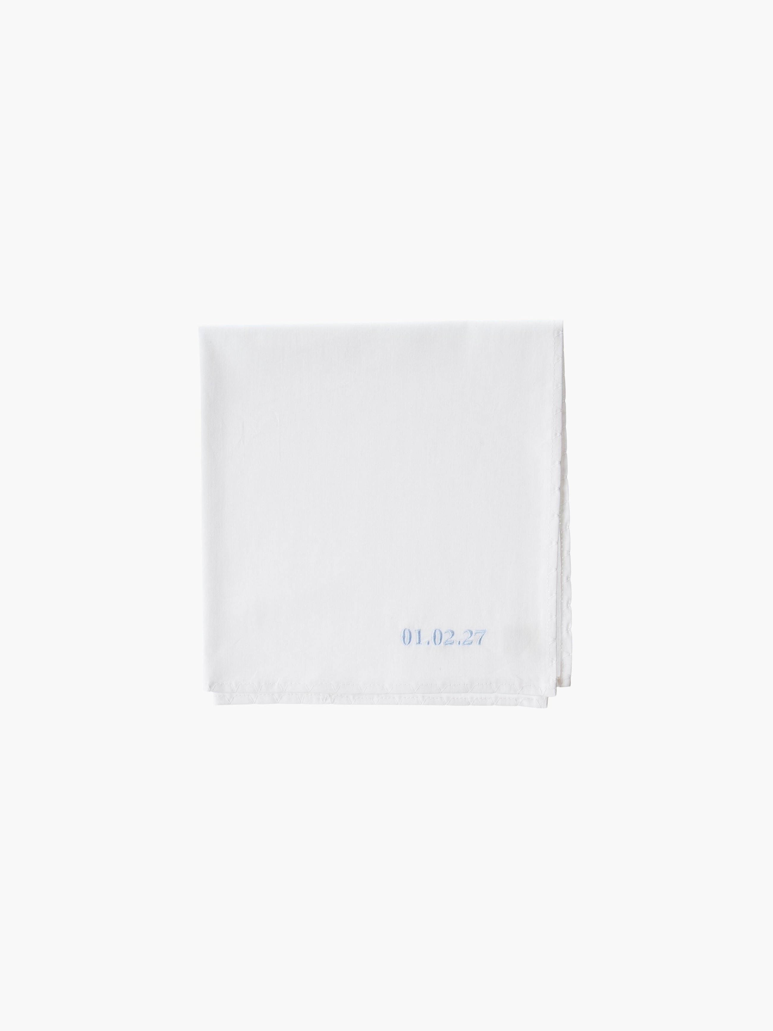 A white cotton embroidered square handkerchief, embroidered with the date in blue.