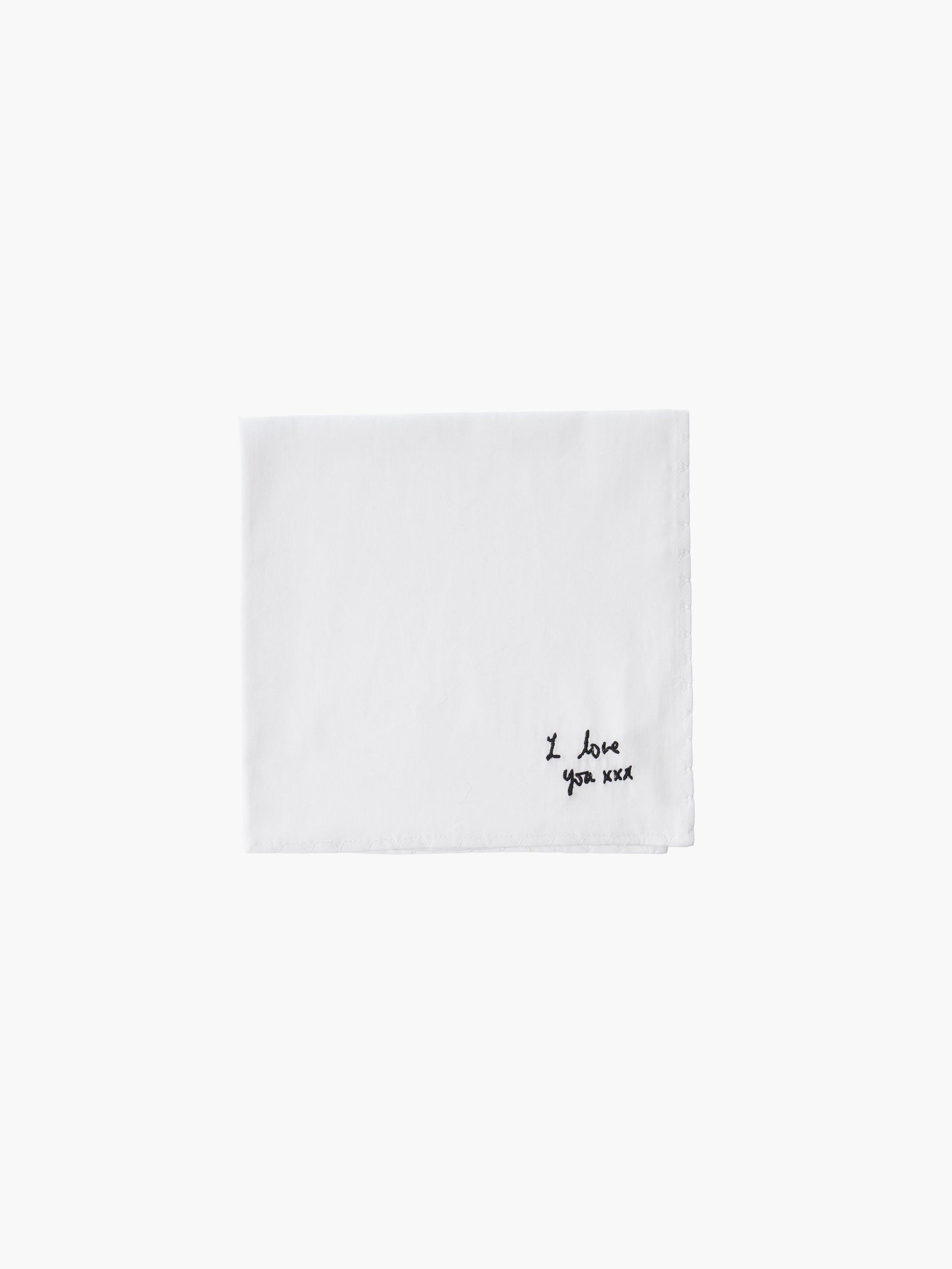 A white cotton embroidered square handkerchief, embroidered with "I love you" in black.