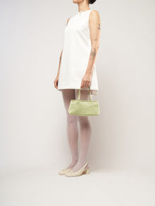 A model wearing a white bridal mini dress, holding a green satin mini handbag.