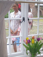 Woman standing behind a window with a vase of flowers in the foreground. They hold small knotted handbags and one wears a large pink scrunchie.